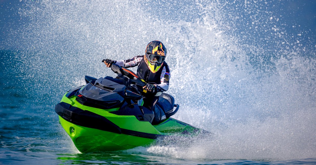 An individual in a black helmet and safety goggles making waves while driving a black and green jet ski.
