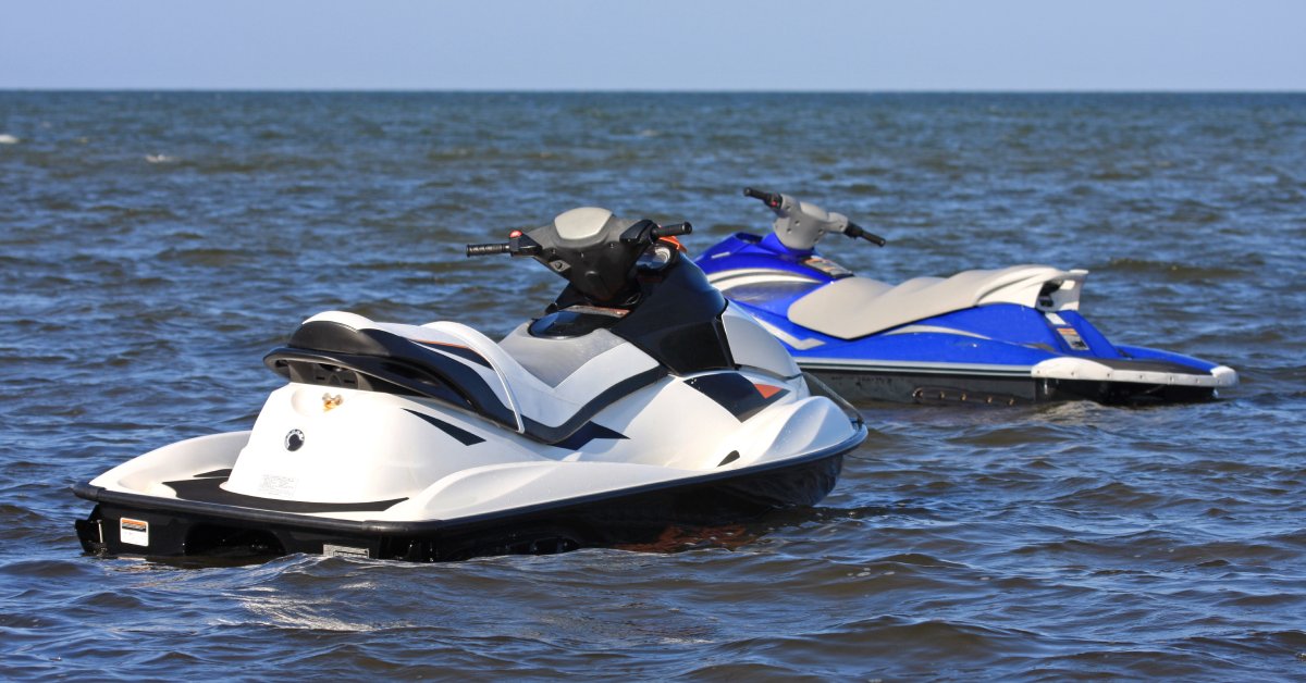 A black and white jet ski and a blue and gray jet ski floating in a large body of water on a sunny day.