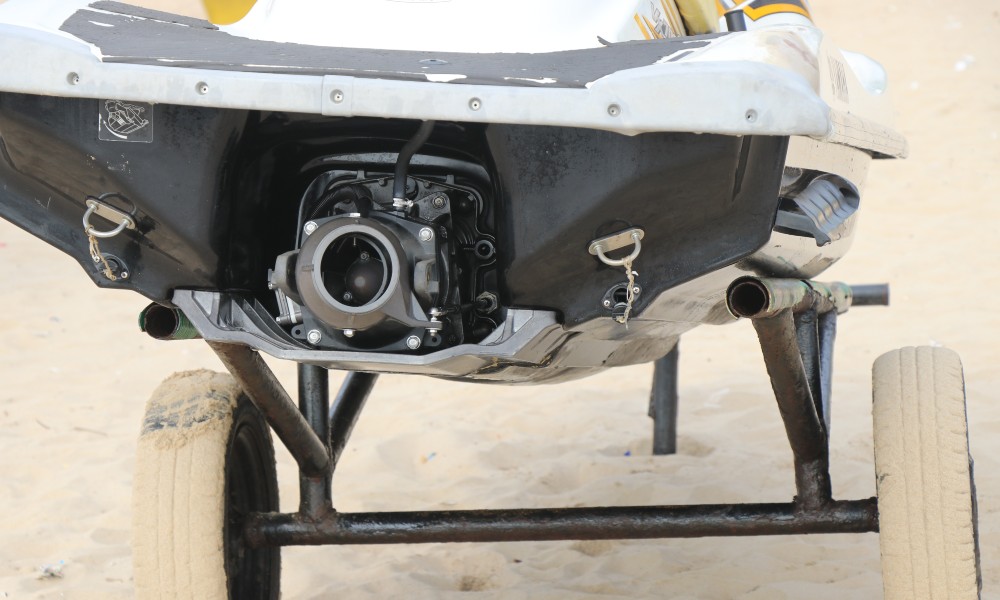 A jet ski sits on a trailer on the beach. The sun is shining bright and you can see the propulsion part of the jet ski