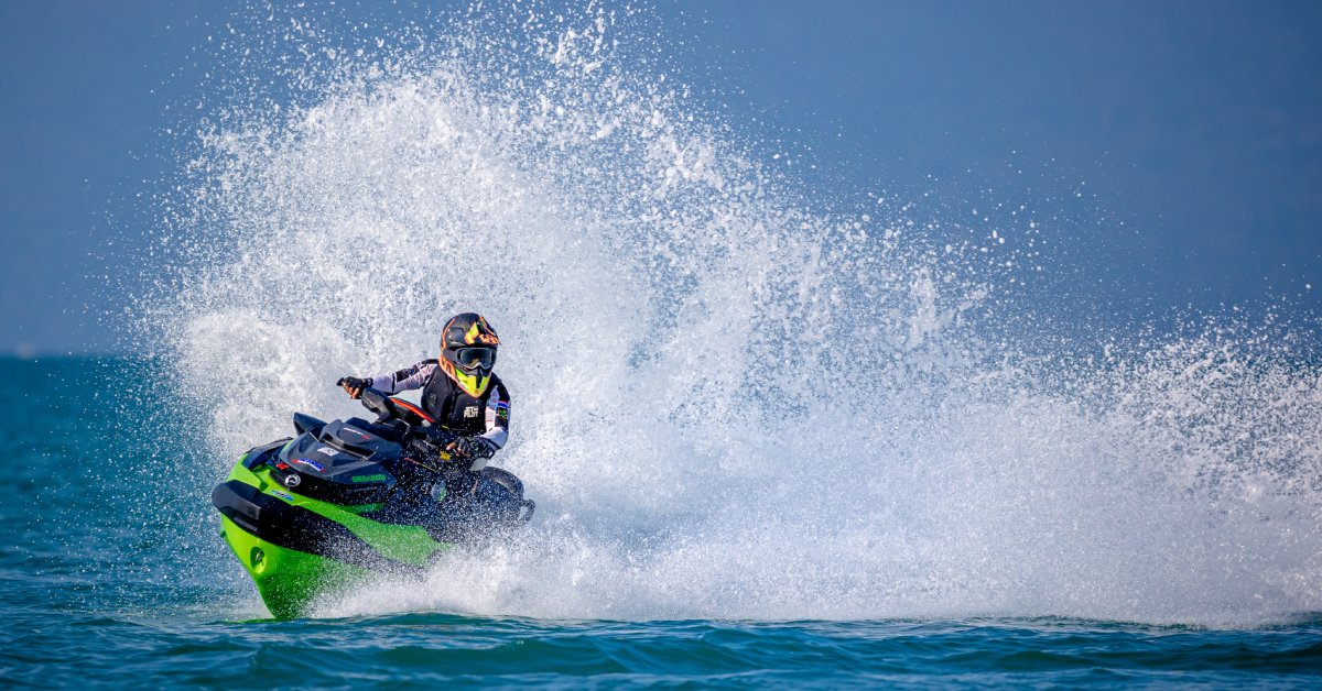 A person out on the water riding a personal watercraft with a safety helmet and life jacket on. They're kicking up water.