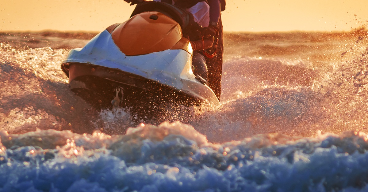 A close-up of a jet ski riding the waves as the sun goes down in the background. The jet ski is red and white.